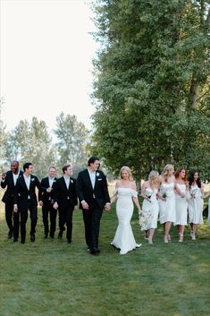 a group of people in formal wear walking through the grass with one person wearing a suit and tie