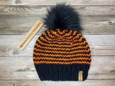 an orange and black knit hat with a fur pom on the top, next to a tag