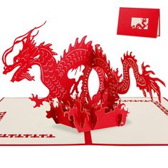 a red paper cut out of a dragon on top of a book with a card in the background