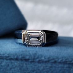 an emerald cut diamond ring sitting on top of a blue velvet cushioned chair with the sky in the background