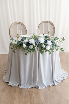 the table is set with white and blue flowers, candles and greenery on it