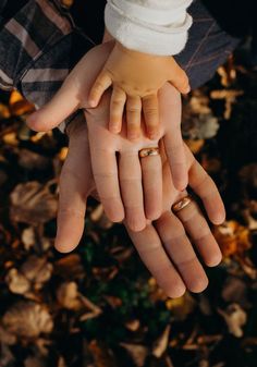 two people holding each other's hands with wedding rings on their fingers in the fall leaves