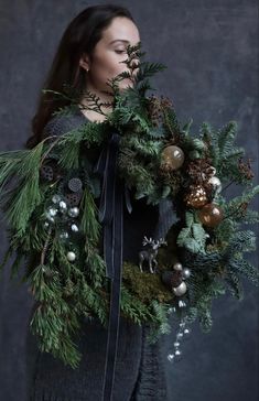 a woman holding a wreath with pine cones and evergreens