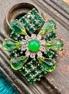 GORGEOUS GREENS! Vintage rhinestone Czech glass button with sparkling green stones and white/clear stone accents.  This one is a stunner! ONLY ONE OF THESE! DON'T MISS OUT ON THIS ONE! Has been in storage for decades. In excellent condition, new old stock. Metal shank.  Please see pic for measurements in inches.  Thank you for stopping by! Green Jeweled Brooches As Gift, Green Jeweled Brooch For Gift, Green Crystal Brooch Jewelry, Green Rhinestone Wedding Brooch, Green Rhinestone Wedding Brooches, Elegant Green Rhinestone Brooches, Vintage Green Rhinestone Brooches, Green Vintage Rhinestone Brooches, Vintage Green Rhinestone Brooch