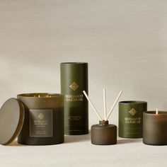 an assortment of candles and diffusers on a table with a white wall in the background