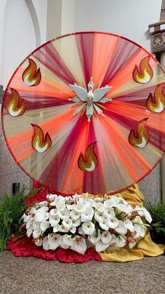 a large red and orange fan sitting on top of a table next to white flowers