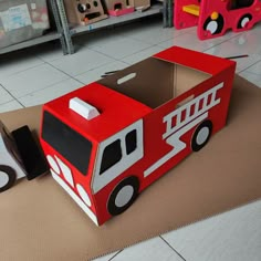 a cardboard box shaped like a firetruck sits on the floor next to other toys