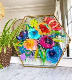 a vase with flowers in it sitting next to a plant on a table near a window