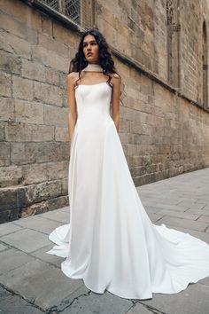 a woman in a white wedding dress standing on the street with her hands behind her back