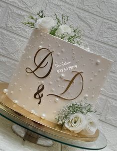 a wedding cake with white flowers and the letter d on top is sitting on a glass platter