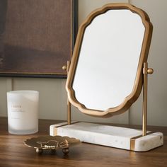 a mirror sitting on top of a wooden table next to a candle and a glass