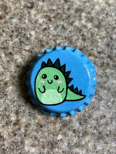 a blue bottle cap with a green dinosaur on it's side sitting on the ground