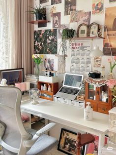 a white desk topped with a laptop computer sitting next to a wall covered in pictures