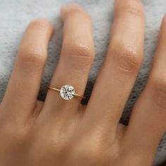 a woman's hand with a diamond ring on top of her finger and white sweater in the background