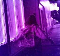 a woman is walking down the street in front of a building with purple lights on it