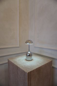 a lamp sitting on top of a wooden block in front of a wall with white paneling