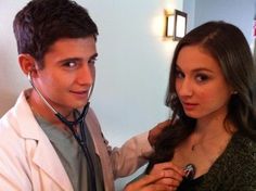 a young woman is listening to a doctor's stethoscope while standing next to a young man