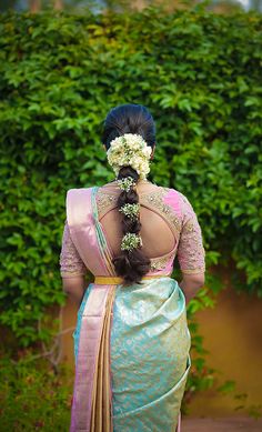 a woman in a blue and yellow sari with flowers in her hair, looking back