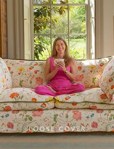 a woman sitting on top of a couch holding a coffee cup in her hands and smiling