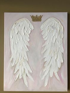 two white angel wings with a gold crown on top are mounted to the wall in front of a beige background