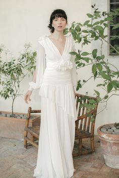 a woman in a white dress standing next to a chair