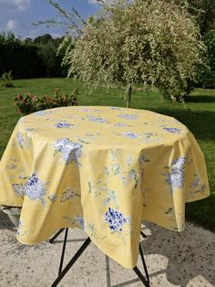 a yellow table cloth with blue and white flowers on it in the middle of a garden