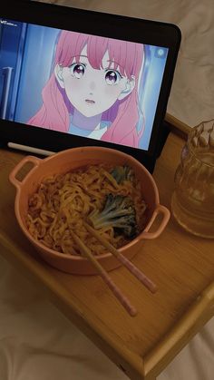 a bowl of noodles and chopsticks on a tray with an ipad in the background