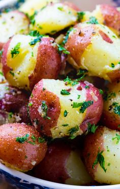 a close up of a bowl of potatoes with parsley on top and seasoning