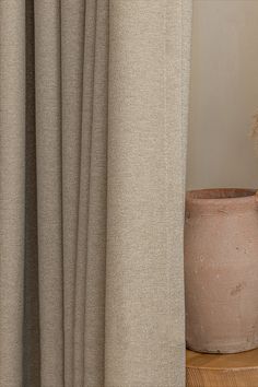 a potted plant sitting next to a curtain in front of a wooden shelf with a vase