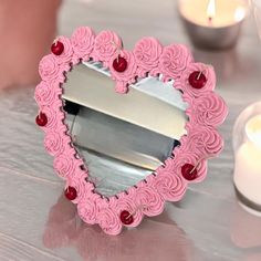 a pink heart shaped mirror sitting on top of a table next to some lit candles