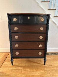 an old dresser is painted black and has gold knobs on the drawers, along with a stair case