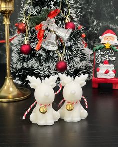 two little white reindeer figurines sitting next to a christmas tree with decorations on it