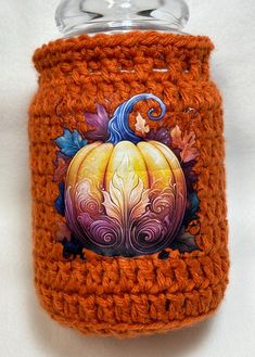 an orange crocheted can holder with a painted pumpkin on the front and side