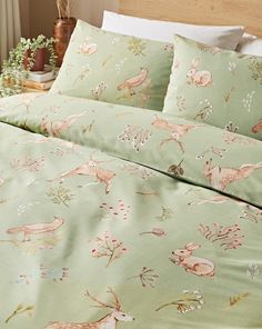 a bed covered in green sheets with deer and flowers on it's coverlet