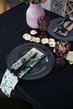 the table is set with black plates and pink vases, silverware, and flowers