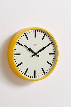 a yellow clock with black hands on a white wall above it is the time eleven o'clock