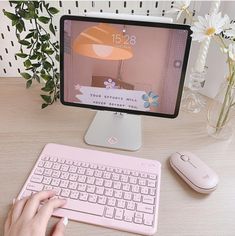 a person typing on a pink keyboard next to a computer monitor and mouse with flowers in the background