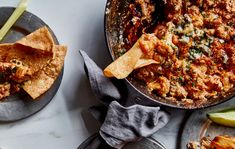 two plates with nachos and an apple on the side, next to a skillet filled with tortilla chips