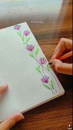 two hands are drawing flowers on a notepad with pencils while another hand is holding a pen