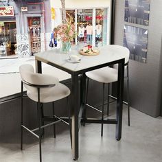 two white chairs sitting at a table in front of a store window with an advertisement on the wall