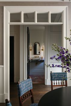 an open door leading to a dining room with blue chairs and purple flowers in vases