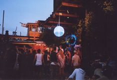 a group of people standing around in front of a building at night with lights hanging from the ceiling