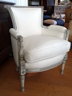 a white chair sitting on top of a hard wood floor next to a wooden dresser