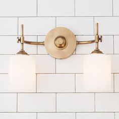 two lights are on the wall in front of white tiles and a light fixture is attached to the wall