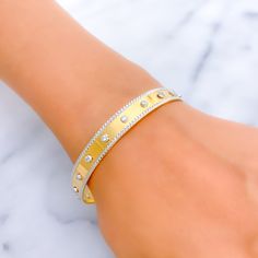 This bangle showcases an exclusive and sleek design, crafted from 22k gold, highlighted by the striking contrast between yellow and white gold finishes. It features a sophisticated embellishment of cubic zirconia stones, adding a touch of brilliance and elegance. Weighing 20.5 grams, this piece combines luxury with a modern aesthetic. The bangle is designed with a size of 2.7 and a bangle opening of 2.45 inches, ensuring a comfortable fit for those with a slightly larger wrist size. Ideal for individuals who seek a blend of contemporary design and timeless materials, this bangle is a standout accessory that complements both casual and formal attire. PRODUCT DETAILS Gold Purity(karat): 22k Item Weight(grams): 20.5 Item Finish: Yellow + White Gold Stone: Cubic Zirconia Size: 2.7 Bangle Openi Modern Gold Bangle With Single Cut Diamonds, Designer Gold Cuff Bracelet With Diamonds, Formal 14k Gold Bangle With Single Cut Diamonds, Luxury Gold Bangle With Brilliant Cut, Designer Diamond Cuff Bracelet In Gold, Designer Gold Bracelets With Brilliant Cut, Modern Hand Set Cubic Zirconia Bangle, Designer Gold Diamond Bangle Bracelet, Modern Gold Bracelet With Single Cut Diamonds