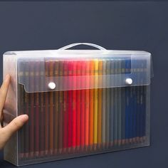 a hand holding a clear box with colored pencils in it