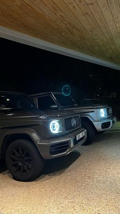 two cars are parked under a wooden structure at night, one is black and the other is silver