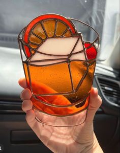 a person holding up a stained glass cup with oranges in the bottom and sides