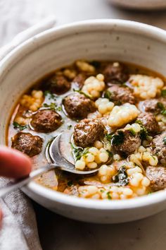 a bowl of soup with meatballs and corn on the cob is being spooned into it