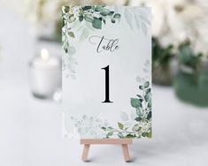 the table numbers are displayed on an easel with greenery and candles in the background